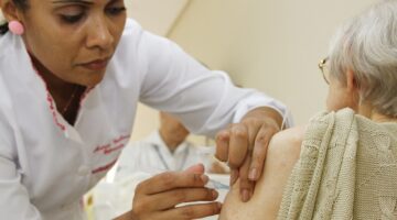 Profissional de saúde aplica vacina em pessoa idosa em unidade de saúde